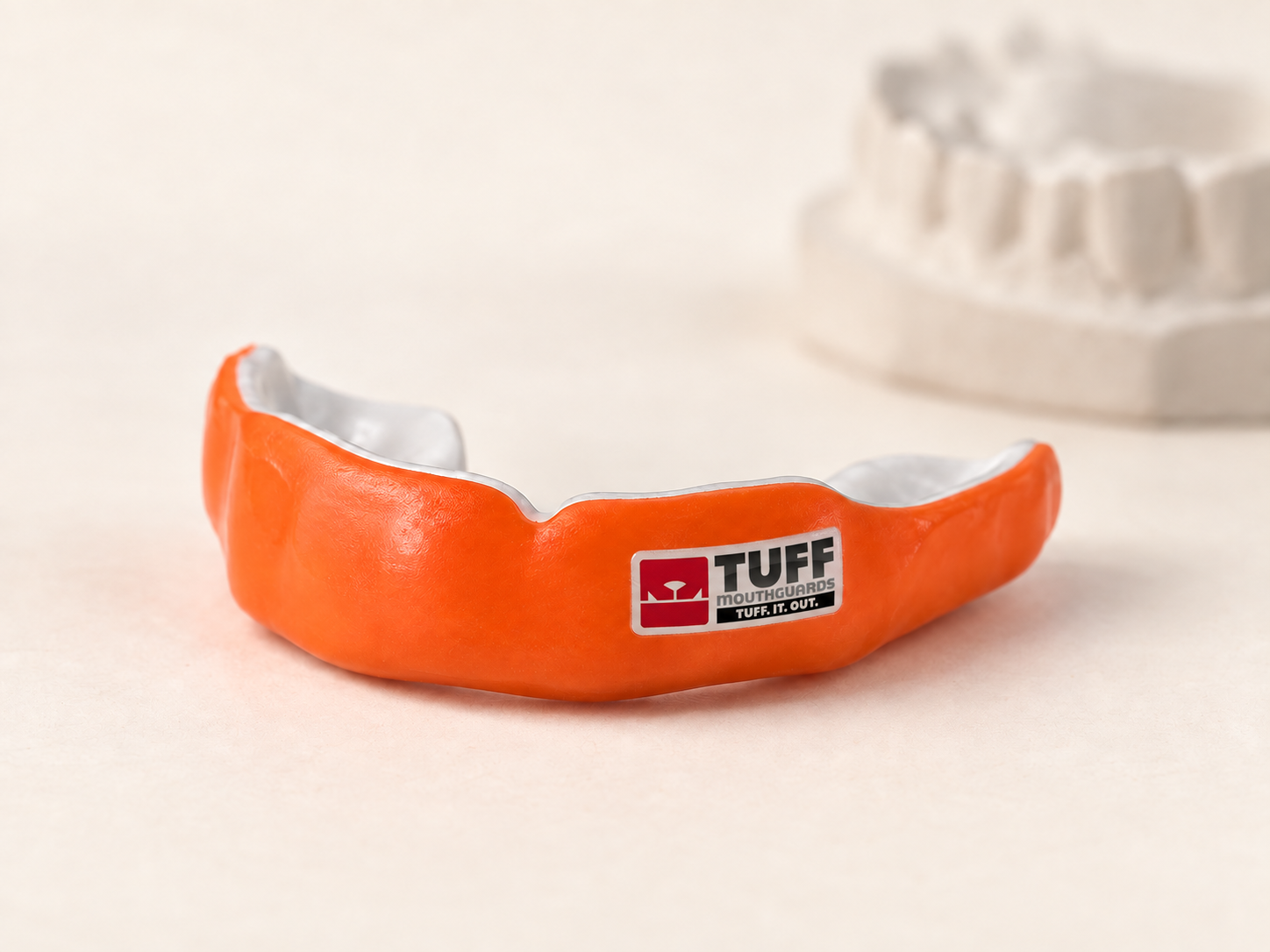 Orange custom sports mouthguard with white lining and a TUFF logo beside a dental model